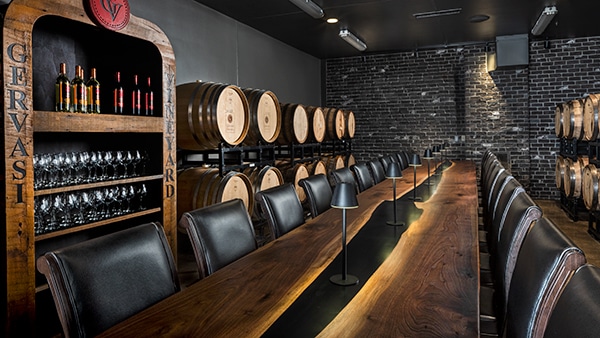 Elegant private dining and wine tasting room at Gervasi Vineyard with wine barrels, leather chairs, and a long wooden table.