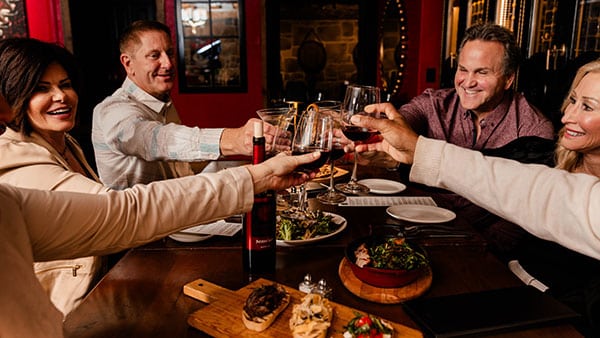Group toasting with red wine around a dinner table at The Bistro at Gervasi Vineyard