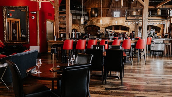 Elegant interior of The Bistro at Gervasi Vineyard featuring rustic wood beams, red bar stools, and a warm, upscale dining ambiance.