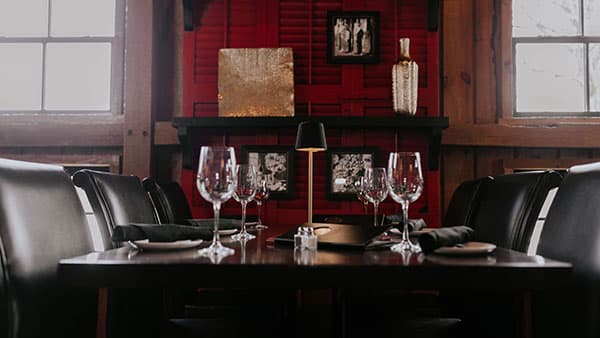 Intimate dining setup at The Bistro at Gervasi Vineyard, featuring elegant glassware, black napkins, and a moody red-accented backdrop.
