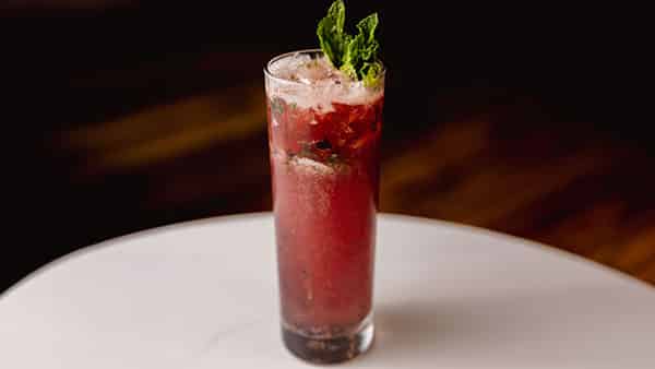 Tall glass of Gervasi Spirits blueberry mojito garnished with fresh mint, served on a marble table at The Still House bar.