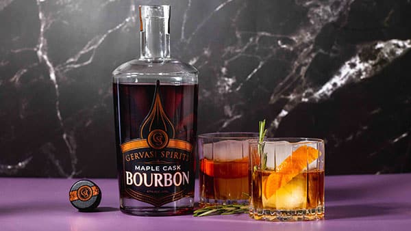 Gervasi Spirits Maple Cask Bourbon with two bourbon cocktails on a purple table, garnished with orange peel and rosemary.