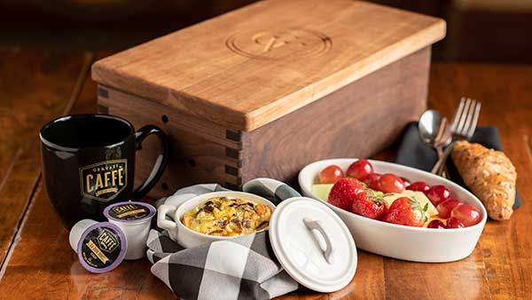 Gervasi Vineyard Italian breakfast box featuring a black coffee mug, single-serve pods, egg casserole, fresh fruit, and a croissant served beside a custom wood box.