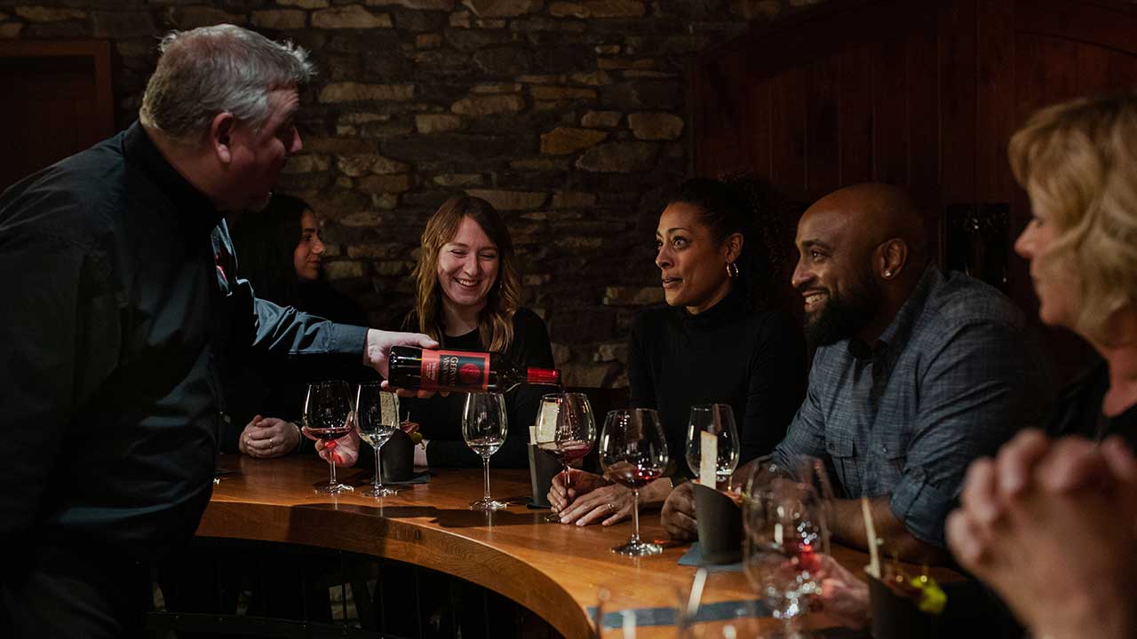 Guests enjoying a wine tasting experience inside The Cave at Gervasi Vineyard, surrounded by stone walls and wine barrels.