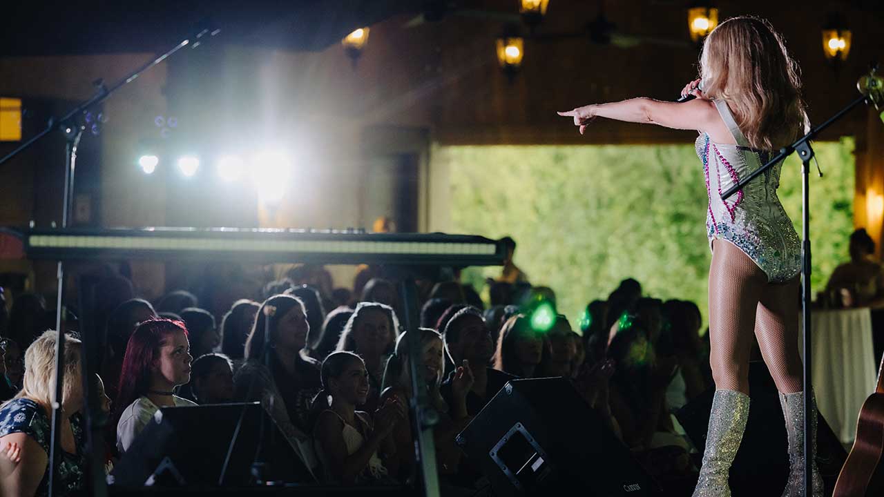 A lively summer concert at Gervasi Vineyard with a performer on stage and an engaged audience under warm lights and open-air ambiance.