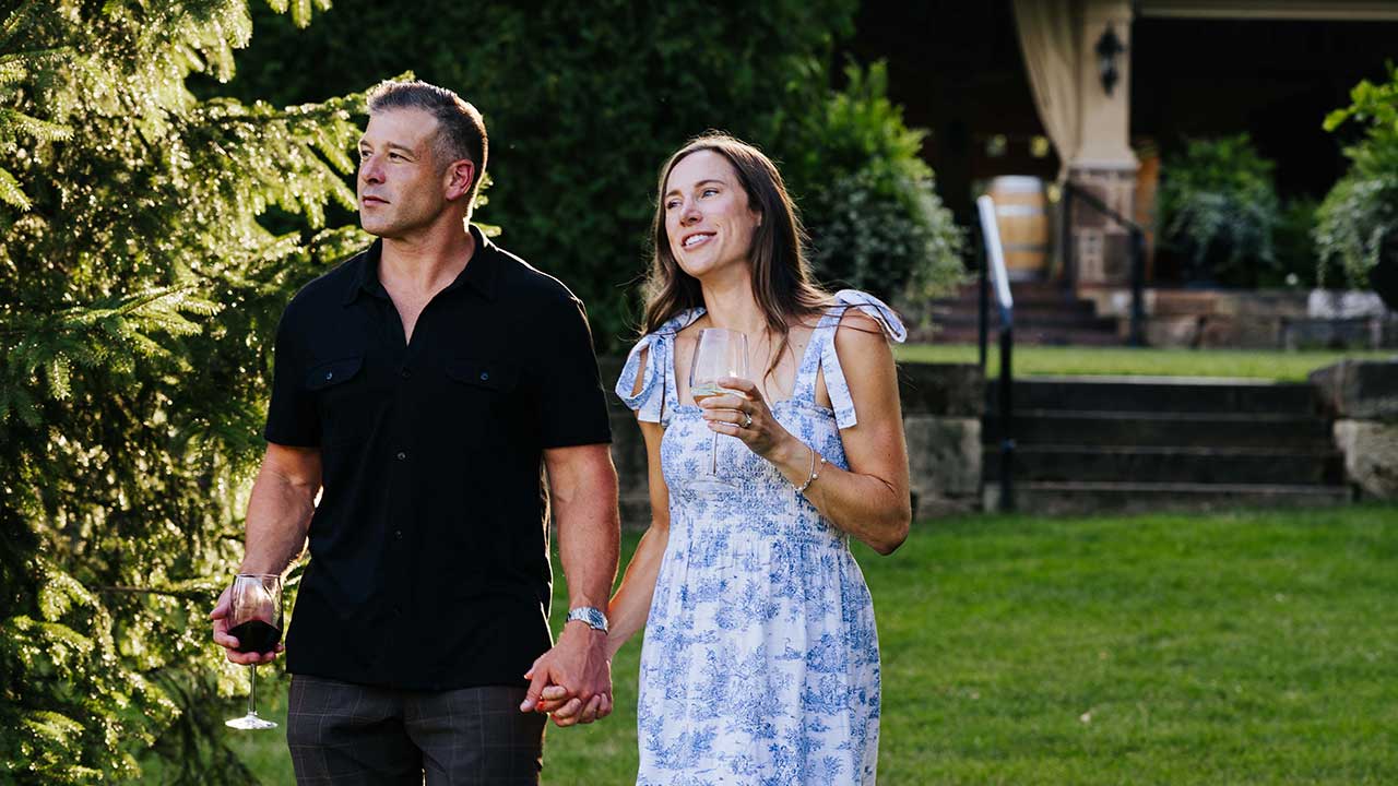 Couple holding hands and sipping wine while strolling through the scenic summer vineyard grounds at Gervasi Vineyard in Canton, Ohio.