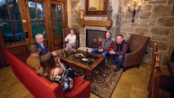Friends enjoying a warm, elegant New Year’s Eve gathering by the fireplace inside a luxurious Gervasi Vineyard villa suite