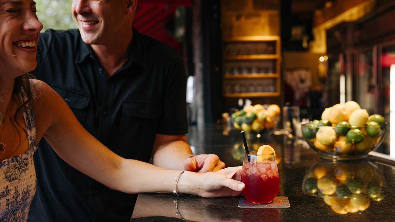 A couple enjoying craft cocktails at a sleek bar inside Gervasi Vineyard, with citrus garnishes and a cozy ambiance highlighting the winery’s casual luxury atmosphere.