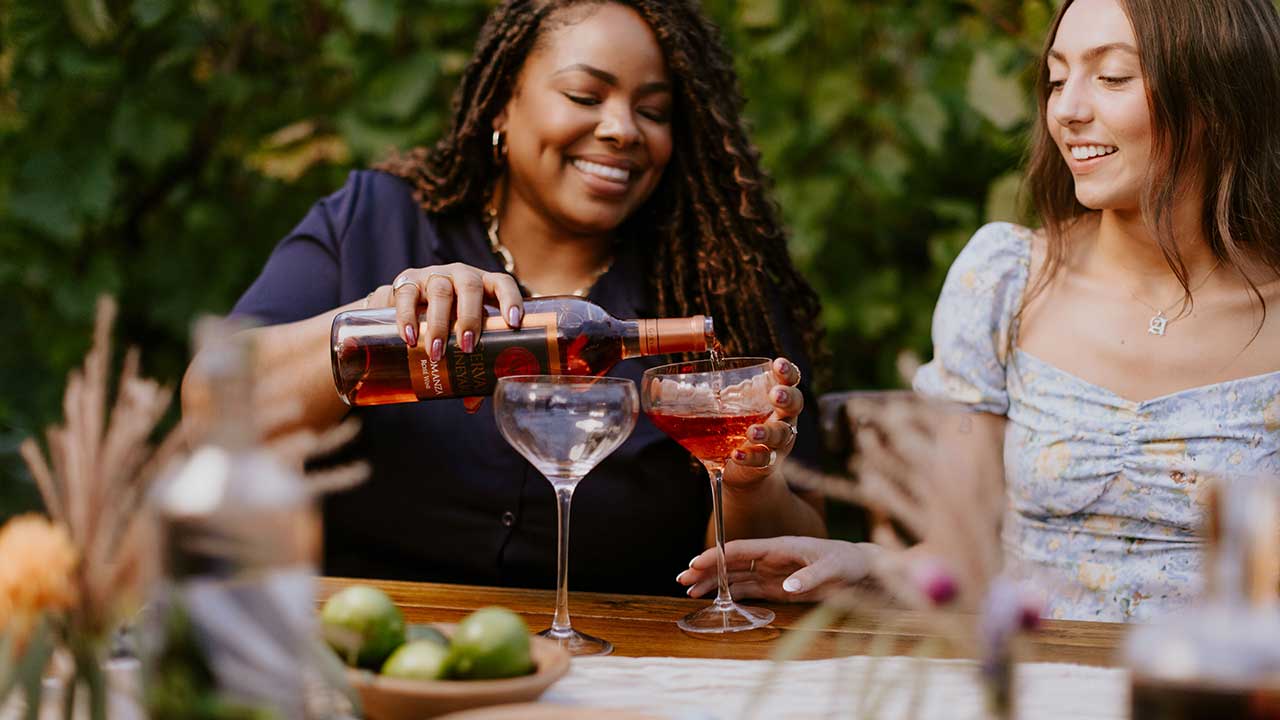 Women enjoying a Gervasi Vineyard wine dinner on the patio, with rosé wine being poured into elegant glasses during a summer evening event.