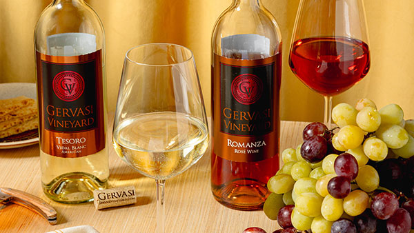 Gervasi Vineyard Tesoro and Romanza wines displayed with white and red wine glasses and fresh grapes on wood table