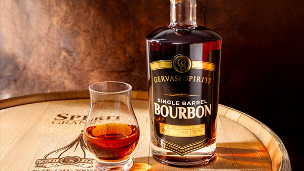 Gervasi Spirits Single Barrel Bourbon bottle and glass on oak barrel with warm lighting