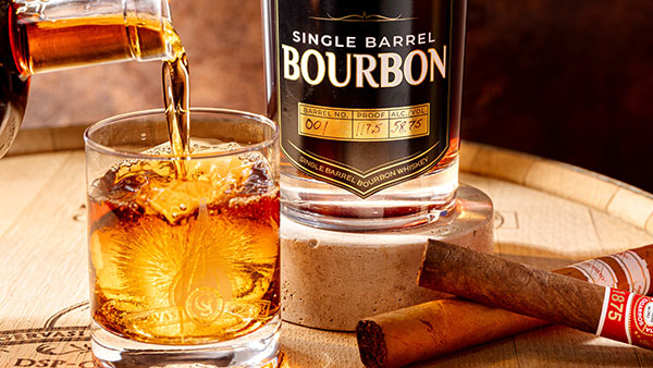 Gervasi Single Barrel Bourbon being poured over ice next to premium cigars on a wooden barrel