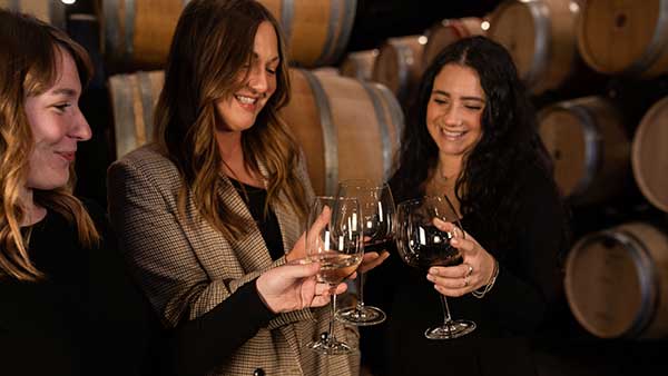 Three women toasting wine in Gervasi Vineyard’s barrel room, celebrating a special occasion.