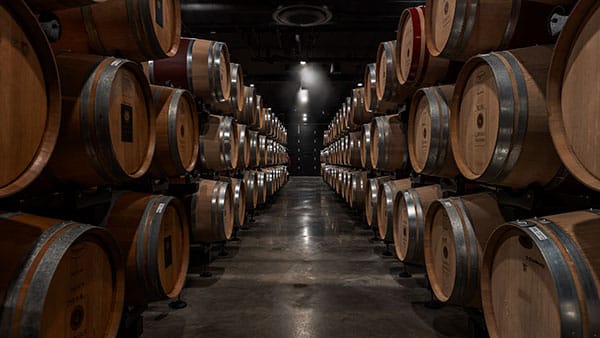 Dimly lit barrel room at The Cave at Gervasi Vineyard lined with stacked aging oak wine barrels.