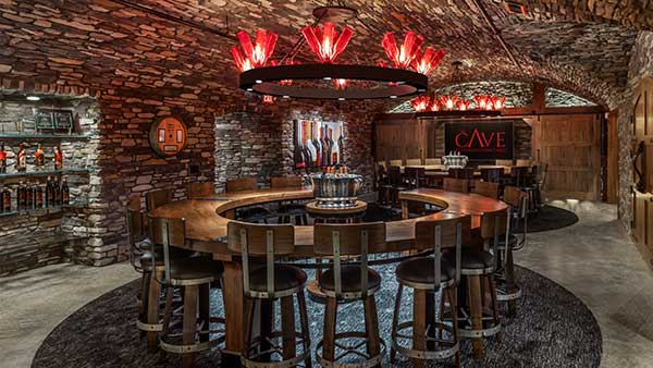 Circular wine tasting bar surrounded by stone walls and red pendant lights inside The Cave at Gervasi Vineyard.