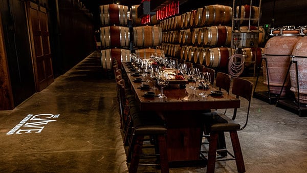 Wine tasting table set inside The Cave at Gervasi Vineyard surrounded by stacked oak barrels and ambient lighting.