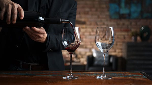 Pouring red wine into a glass during a tasting session at Gervasi Vineyard, with a rustic brick wall in the background.