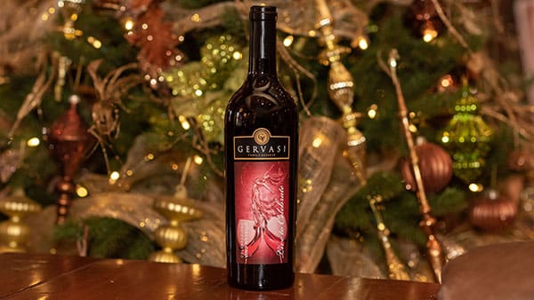 Gervasi Vineyard Celebrazione red wine bottle displayed in front of an elegant, gold-lit Christmas tree during the holiday season