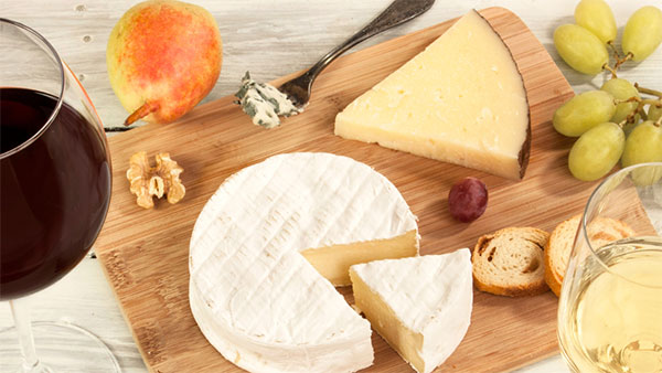 Red and white wine glasses paired with soft and aged cheeses, fruit, and crackers on a wooden cutting board