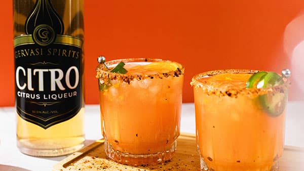 Gervasi Spirits Citro citrus liqueur with two orange jalapeño cocktails rimmed with chili salt on a wooden board