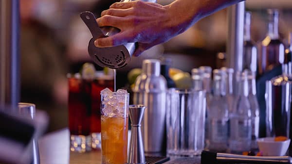 Bartender crafting a cocktail at Gervasi Vineyard’s distillery bar, pouring from a shaker into an ice-filled glass