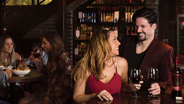 Guests sharing wine and conversation at The Bistro at Gervasi Vineyard, surrounded by rustic wine cellar ambiance.