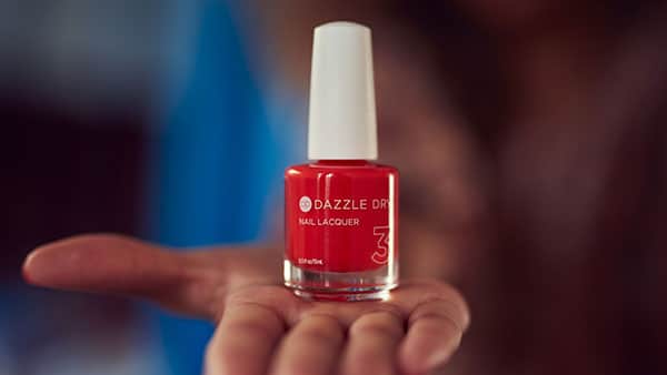 Close-up of a hand holding a bottle of Dazzle Dry red nail lacquer, now available at The Spa at Gervasi Vineyard.