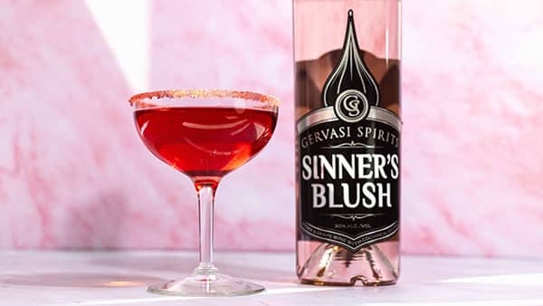 Gervasi Spirits Sinner’s Blush cocktail with sugar rim and rich red hue, displayed alongside the signature bottle on a pink marble surface