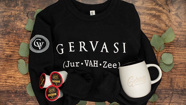 Gervasi Vineyard branded sweatshirt, mug, and coffee pods arranged on a rustic wood table, perfect for cozy holiday gifts.