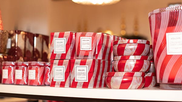 Holiday collection of Voluspa crushed candy cane candles in red and white packaging on a shelf at The Marketplace at Gervasi Vineyard.