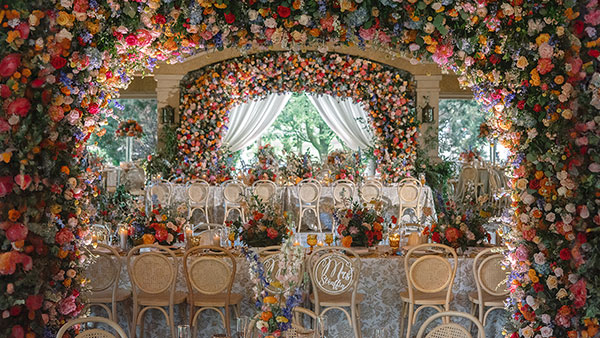Lavish outdoor wedding reception at Gervasi Vineyard under a vibrant floral arch with ornate seating and table decor.