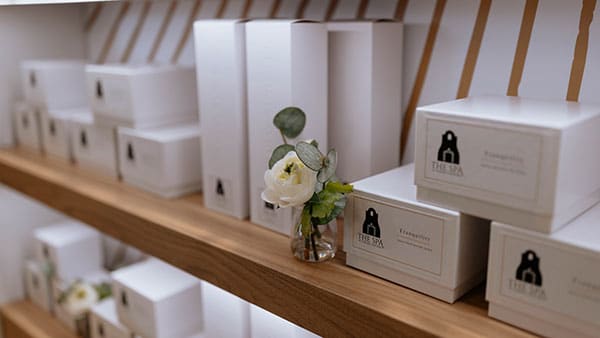 Gift boxes and spa essentials from The Spa at Gervasi Vineyard displayed on wooden shelves with elegant floral accents.