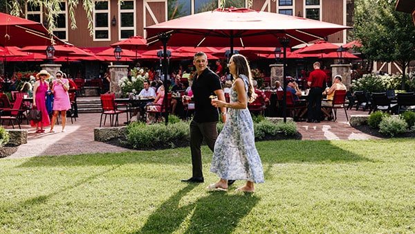 Guests strolling across the lawn near Gervasi Vineyard’s Piazza patio with red umbrellas during summer