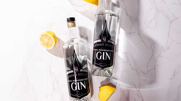 Overhead view of two Gervasi Spirits Pink Peppercorn Gin bottles with fresh lemon wedges on a marble background.
