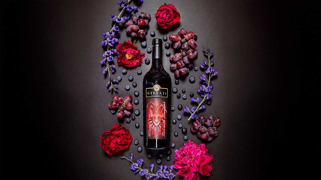 A bottle of Gervasi’s Risata Red Sangria surrounded by grapes, blueberries, and vibrant floral elements, illustrating the fruity and aromatic profile of this small-batch wine.