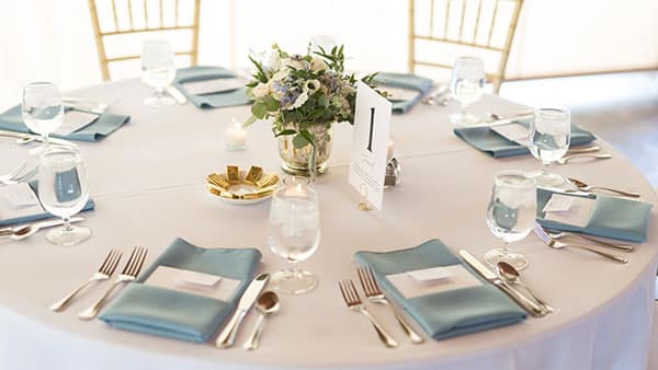 Close-up of a round wedding reception table with light blue napkins, floral centerpiece, and elegant place settings at Gervasi Vineyard.