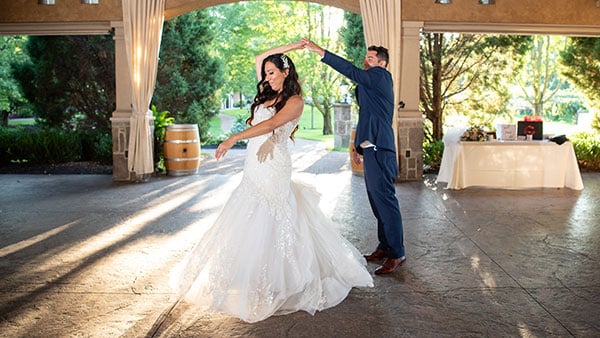 Bride and groom share their first dance in an open-air pavilion at Gervasi Vineyard, bathed in golden sunlight.