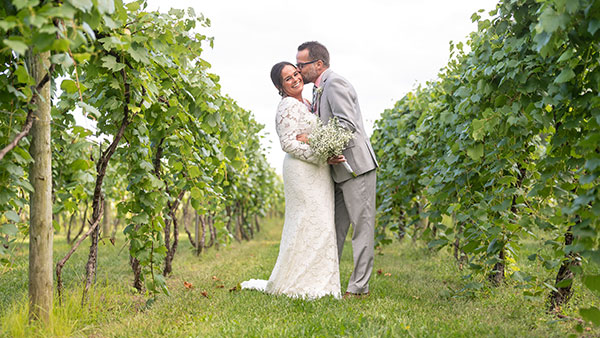 Newlyweds embracing in the vineyard rows at Gervasi Vineyard, surrounded by lush green vines.
