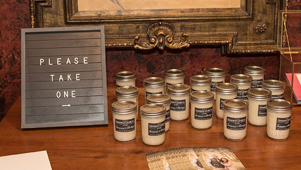 Rustic wedding favor display with candles in mason jars and a sign inviting guests to take one at Gervasi Vineyard.