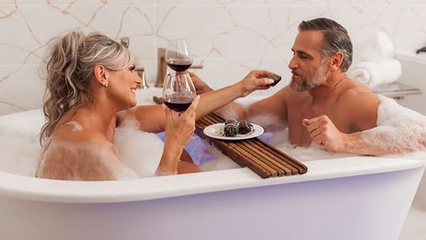 A couple relaxes in a luxurious soaking tub at The Spa at Gervasi Vineyard, enjoying wine and chocolate-covered strawberries during a romantic couples retreat.