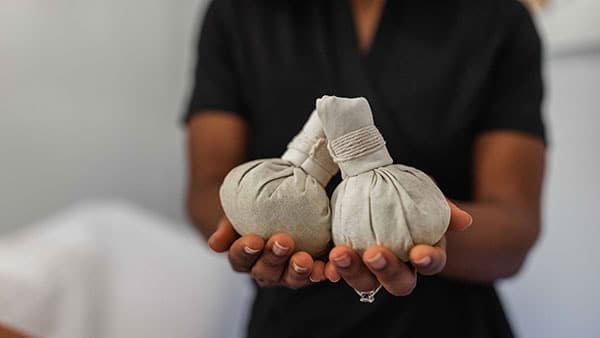 Therapist holds warm herbal compresses used in holistic spa treatments at Gervasi Vineyard, offering natural relaxation and muscle relief.
