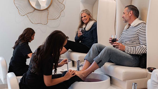 Couple enjoying side-by-side pedicures with wine at The Spa at Gervasi Vineyard, highlighting Dazzle Dry services in a spa experience.