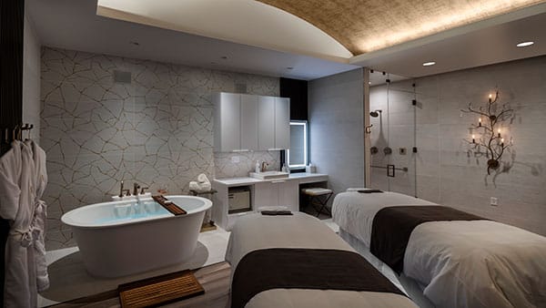 Luxury treatment room at The Spa at Gervasi Vineyard featuring a soaking tub, dual massage tables, and a modern walk-in shower.