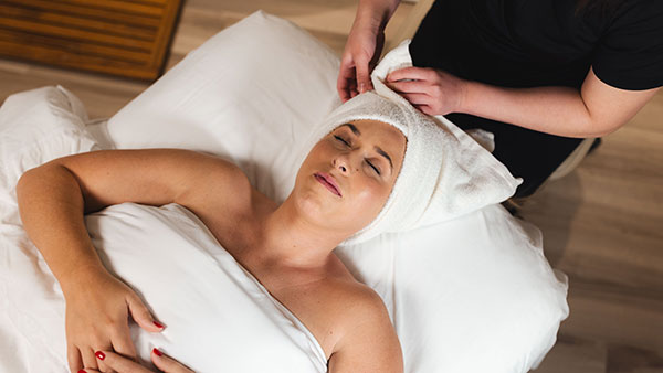 Woman receiving a soothing facial wrapped in a towel at The Spa at Gervasi Vineyard, highlighting rejuvenating skincare experiences.