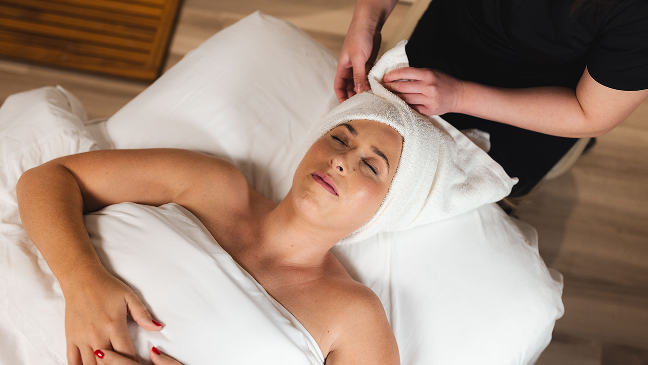 A woman receives a head wrap and relaxing facial treatment at The Spa at Gervasi Vineyard, capturing the peaceful ambiance and rejuvenating summer spa experience in Canton, Ohio.