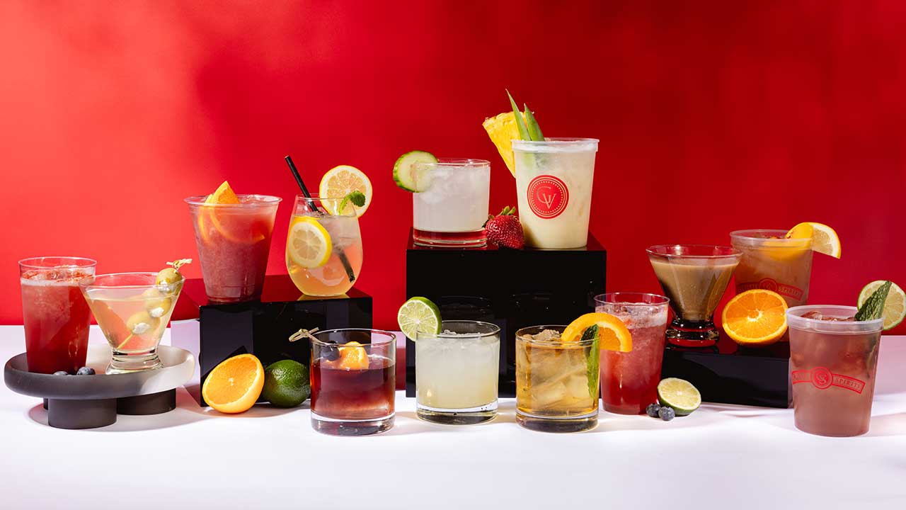 Colorful array of Gervasi Vineyard signature summer cocktails displayed on a white and red backdrop, featuring citrus garnishes and a variety of glasses for refreshing warm-weather drinks.