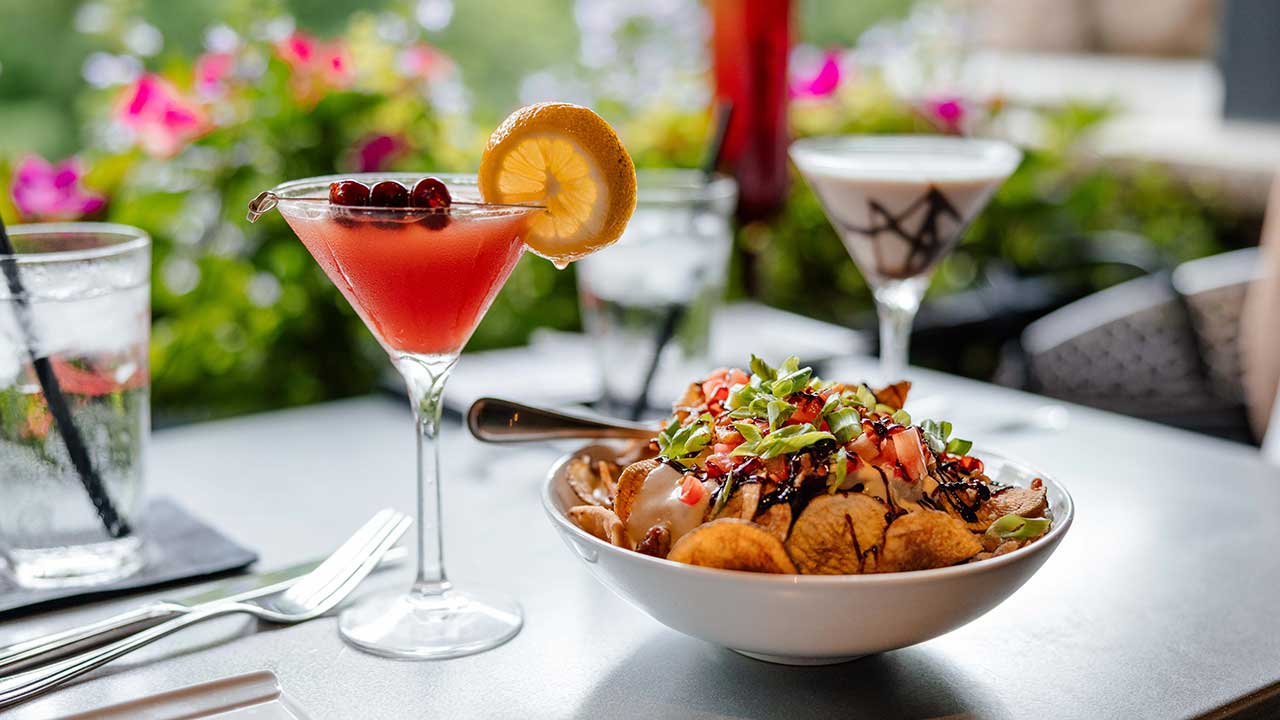 Cocktail and appetizer pairing at Gervasi Vineyard, featuring a fruity martini with lemon and a gourmet dish of chips topped with tomato, cheese, and herbs.