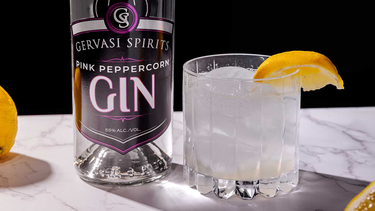 Gervasi Spirits Pink Peppercorn Gin bottle next to a simple gin cocktail with lemon slice on a marble surface, highlighting a bold twist on a summer classic in Canton, Ohio.