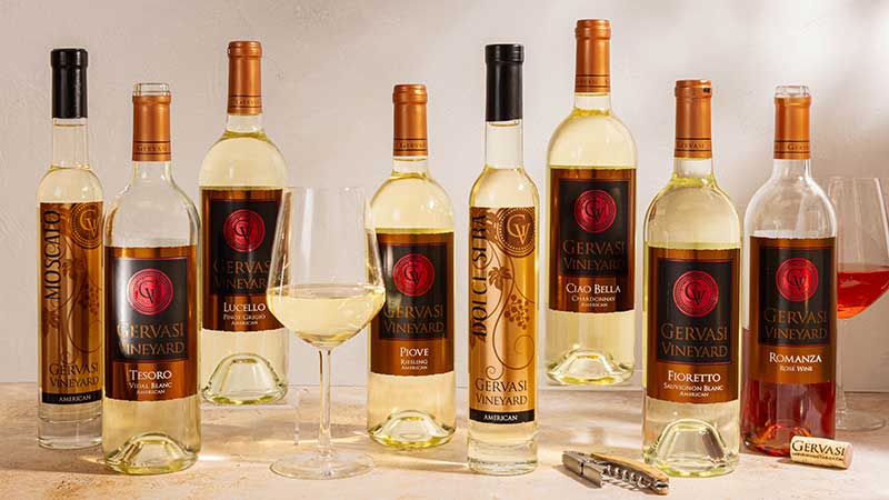 A full lineup of Gervasi Vineyard white wines including Moscato, Tesoro, Lucello, Piove Riesling, Dolce Sera, Ciao Bella Chardonnay, Fioretto Sauvignon Blanc, and Romanza rosé, elegantly displayed with wine glasses, ideal for summer sipping in Canton, Ohio.