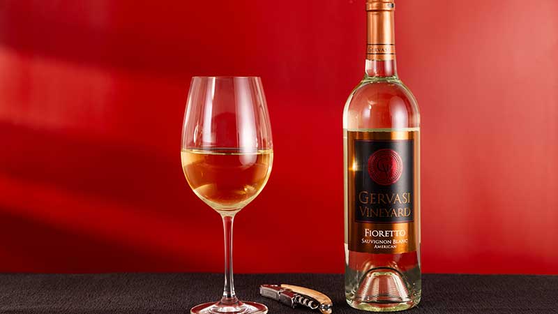 A bottle of Gervasi Vineyard Fioretto Sauvignon Blanc paired with a filled glass, wine opener, and a bold red backdrop, highlighting crisp white wine perfect for summer evenings in Canton, Ohio.